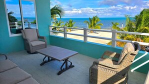 A balcony with wicker furniture, a view of the beach, and a turquoise wall. - Island Magic Villas (Caye Caulker)