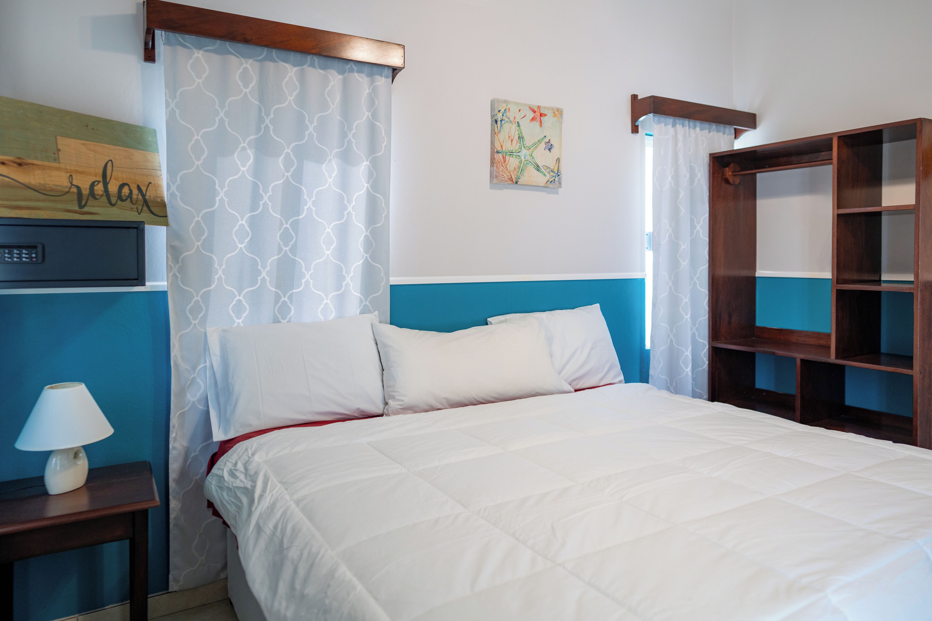 Una cama bien hecha con ropa blanca, una mesita de noche con lámpara y un armario de madera con estantes abiertos.