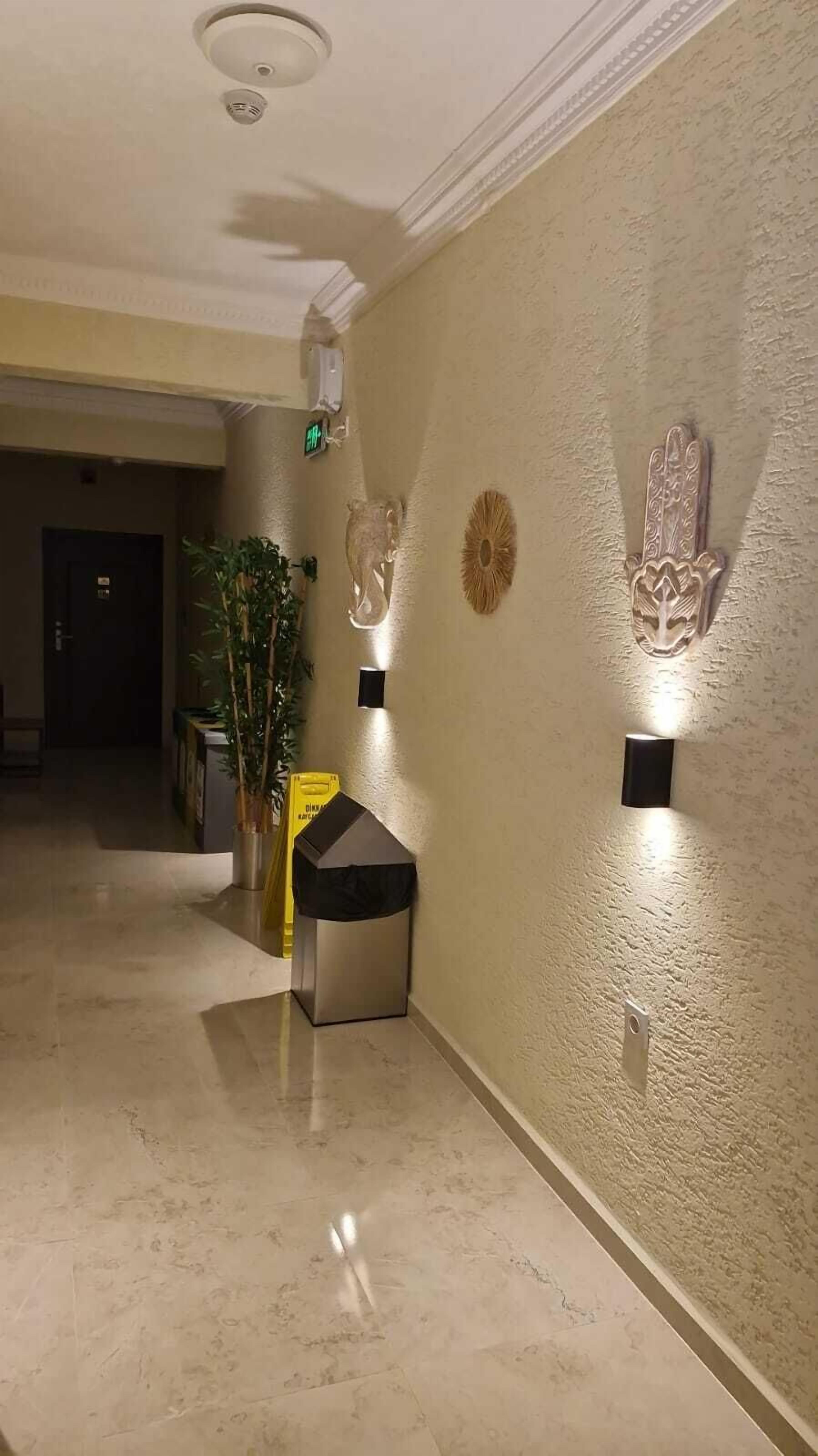 Um corredor com piso de mármore, um vaso de planta, um pequeno banco e arte decorativa na parede.