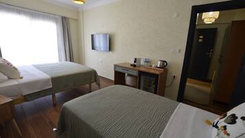 A hotel room with two beds, a desk with a refrigerator, a television, and a door to a bathroom.