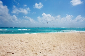 A sandy beach with clear blue water and a few people in the distance.