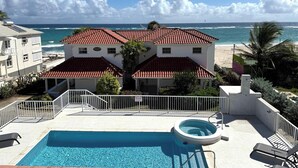 Um edifício de dois andares com telhado de telhas vermelhas, piscina e vista para o oceano.