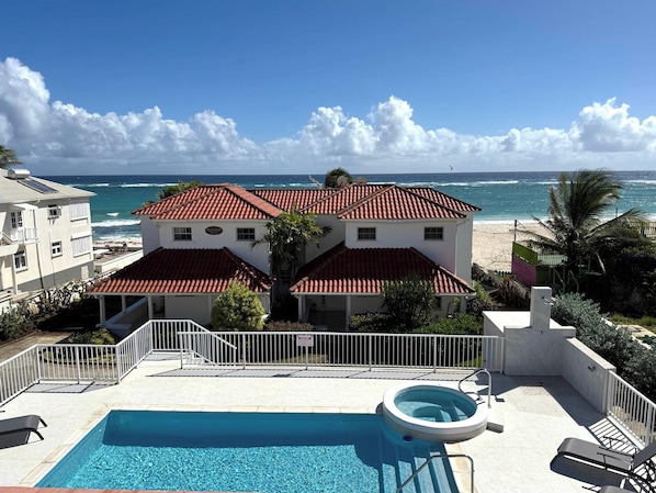 A two-story building with a red-tiled roof, a swimming pool, and a view of the ocean.