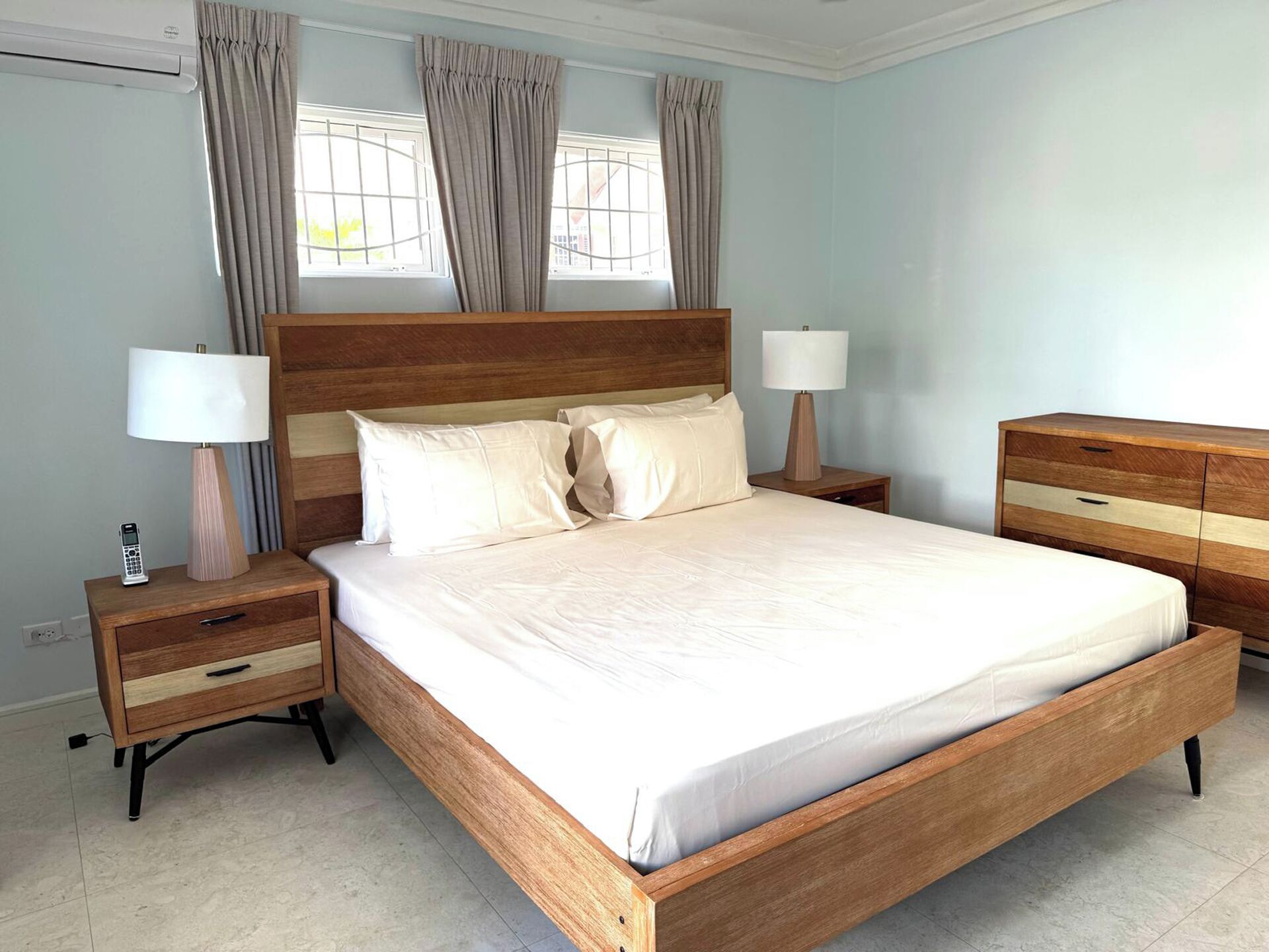 A bedroom with a wooden bed, two bedside tables with lamps, a nightstand, and a dresser.