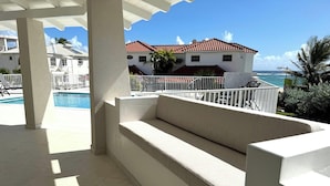 Uma área de estar coberta ao ar livre com uma piscina ao fundo.