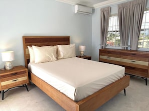 A bedroom with a wooden bed, bedside tables, a dresser, and a window with curtains.
