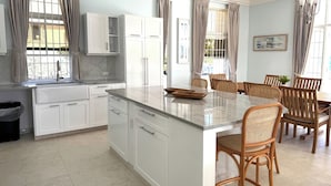 Uma cozinha moderna com armários brancos, bancada de mármore e área de jantar com cadeiras e mesa de madeira.