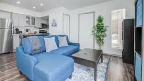 A modern living room with a blue sofa, a coffee table, and a kitchen in the background.