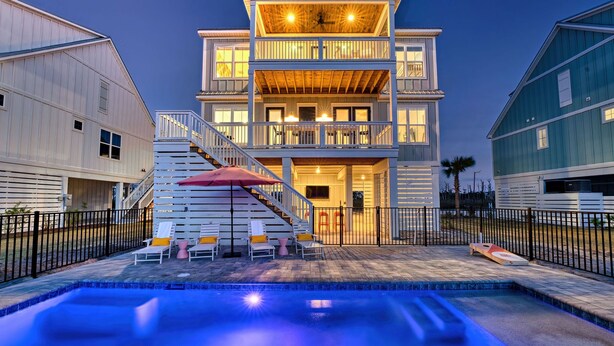 A multi-story building with a pool area, outdoor seating, and a staircase leading to the entrance.
