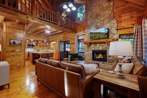 Un intérieur de cabane spacieux, doté d’une cheminée en pierre, de meubles en bois et d’un coin cuisine.