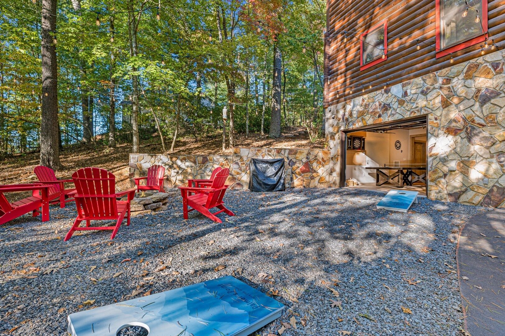Un chalet rustique à l’extérieur en pierre, avec un mur en pierre et une terrasse en gravier agrémentée de chaises Adirondack rouges.