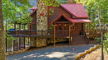 A log cabin with a stone foundation, a red metal roof, and a wooden deck with railings.