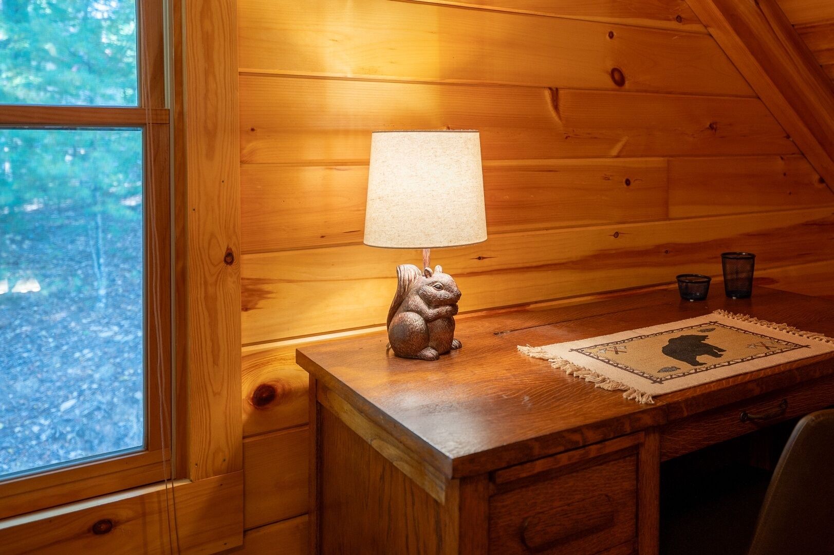 A wooden interior with a lamp on a table, a window, and a small rug with a bear design.