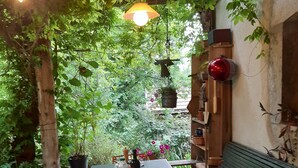 Un espace de restauration en plein air avec une table dressée pour deux personnes, entouré de verdure et agrémenté d’un banc en bois.