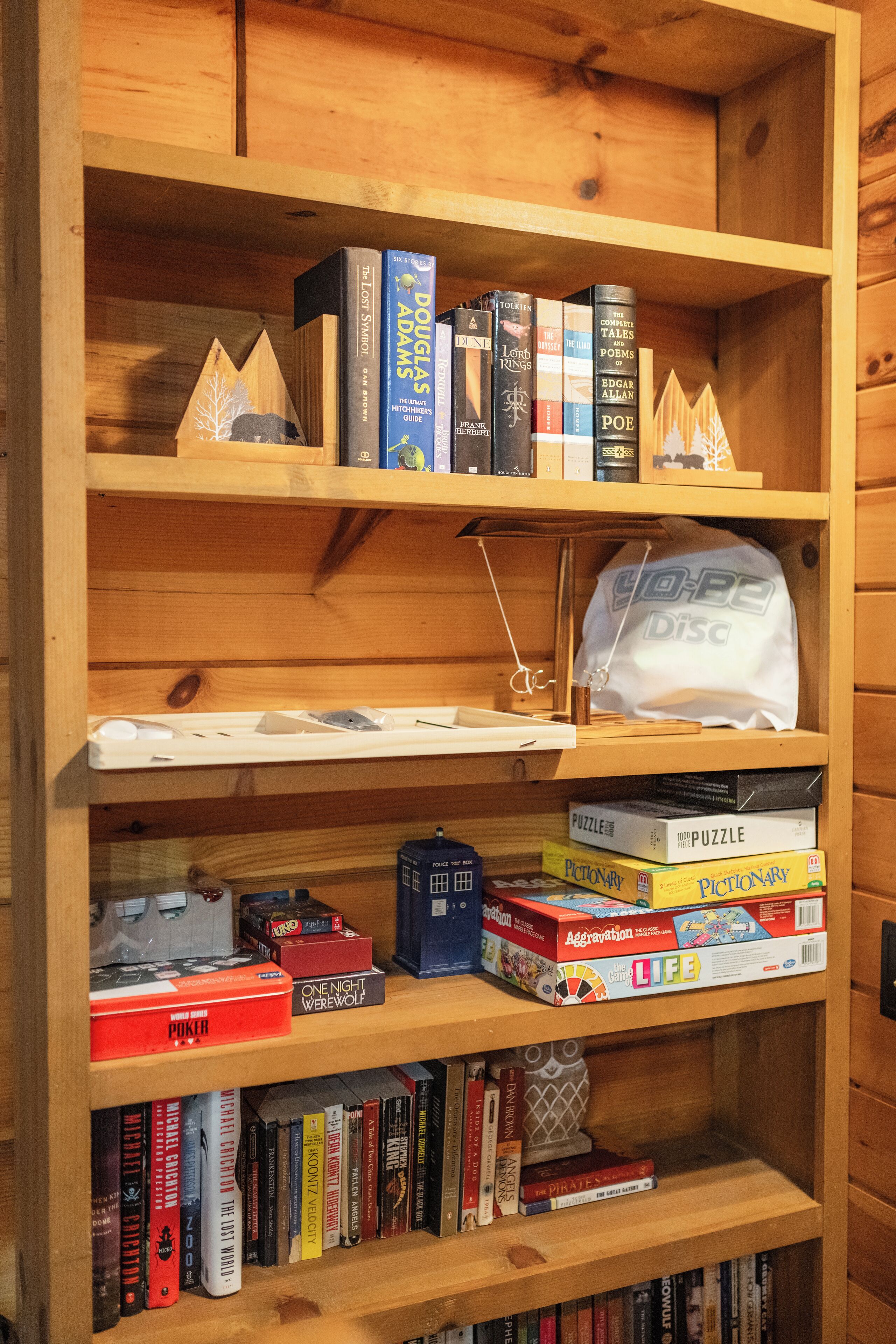 A wooden bookshelf with various books, puzzles, and a disc bag.