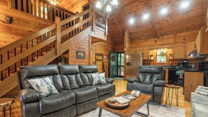 A spacious living area with a leather sofa, a wooden coffee table, and a staircase leading to an upper level. - Hot Tub--Pet-Friendly--Rustic River-View Cabin (Cherry Log)