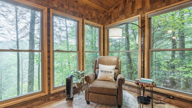 A cozy room with a large window, a plush armchair, a standing lamp, and a small table. - Hot Tub--Pet-Friendly--Rustic River-View Cabin (Cherry Log)