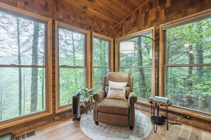 Una habitación acogedora con un ventanal grande, un sillón cómodo, una lámpara de pie y una mesita pequeña.