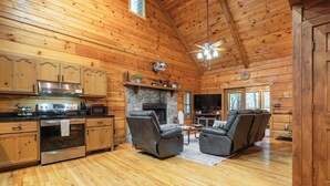 A log cabin interior with a kitchen, fireplace, two leather recliners, and a television. - Hot Tub--Pet-Friendly--Rustic River-View Cabin (Cherry Log)