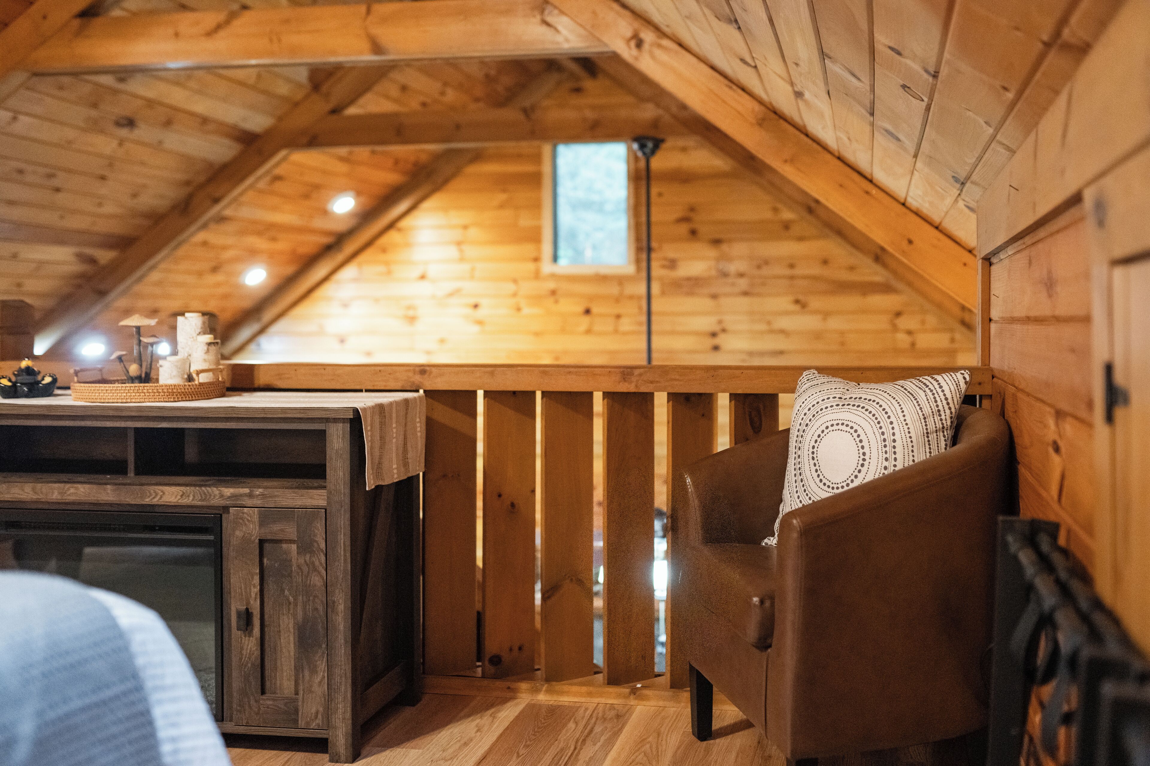 Interior acogedor de una cabaña de madera con cama en altillo, una mesita con velas y una ventana que deja entrar luz natural.