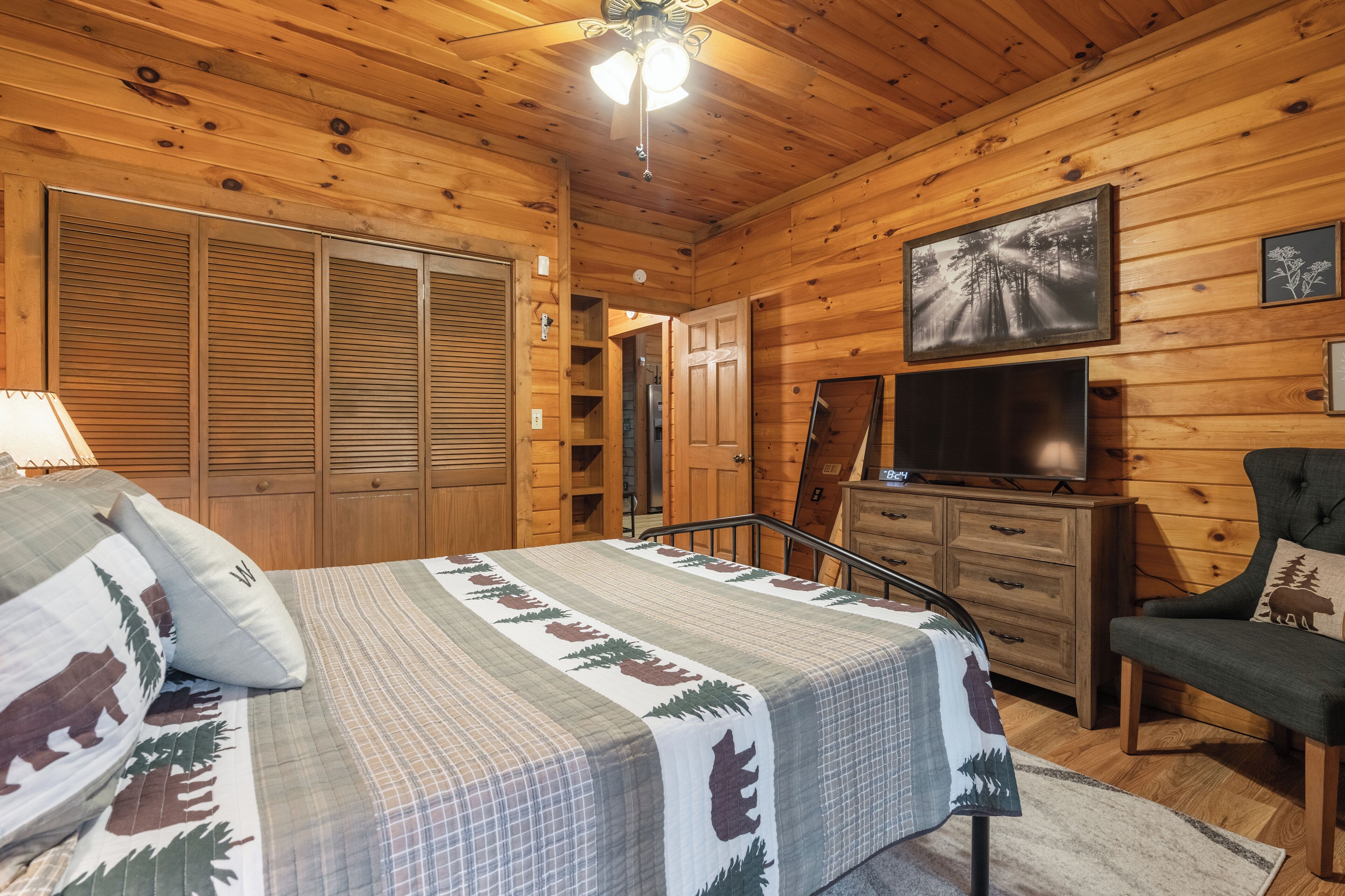 A wooden cabin bedroom with a bed, a dresser, a chair, a television, and a closet.
