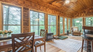 A cabin interior with large windows, wooden floors, a ceiling fan, a fireplace, and a cozy seating area. - Hot Tub--Pet-Friendly--Rustic River-View Cabin (Cherry Log)