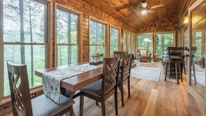 A wooden cabin with large windows, a dining table, and a bar area. - Hot Tub--Pet-Friendly--Rustic River-View Cabin (Cherry Log)