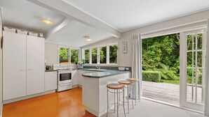 A modern kitchen with a large island, white cabinetry, and a view of a lush garden through large windows. - Fisherman’s retreat in Turangi (Turangi)
