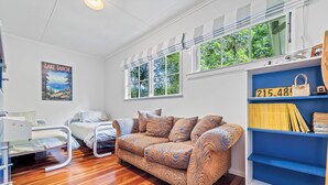 A room with a wooden floor, a patterned sofa, a bed, a window with a view of trees, and a shelf with a handbag and a sign. - Fisherman’s retreat in Turangi (Turangi)