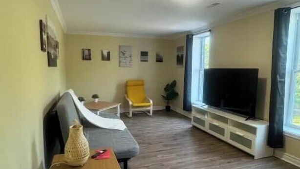 Ein Wohnzimmer mit einer Couch, einem gelben Sessel, einem Fernseher und Holzböden.