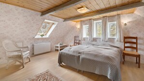 Een slaapkamer met een schuine balklaag, een groot bed, twee houten stoelen, een kleine tafel en een radiator.
