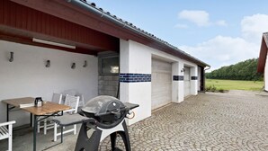 Een gebouw met een garagepoort, een terras met een tafel en stoelen, en een barbecue.