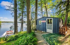 Ein kleines Häuschen mit dem Schild "Half Way House", umgeben von hohen Bäumen und Blick auf einen See.