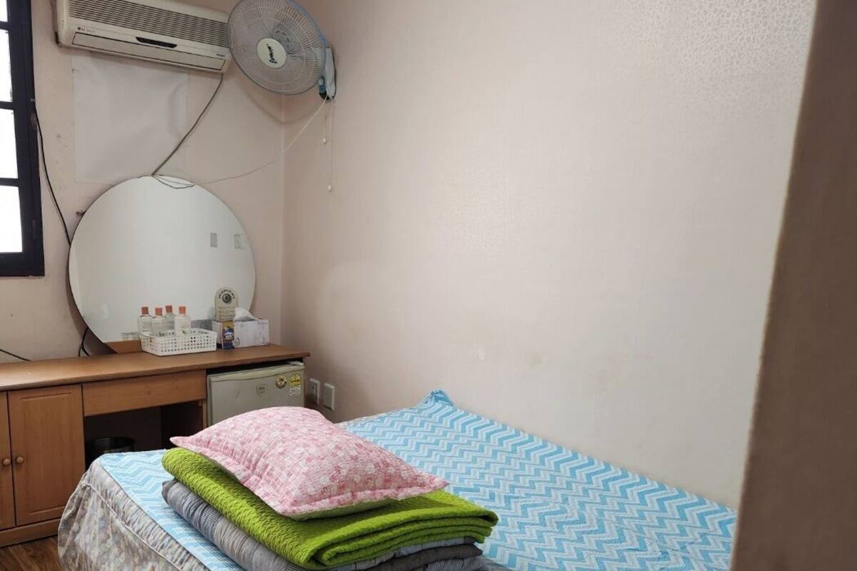 A small, tidy room with a bed, a desk, and a wall-mounted air conditioner.