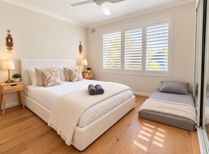 Ein Schlafzimmer mit einem großen Bett, Nachttischen, einer Nachttischlampe, einem Fenster mit Jalousien und einem Deckenventilator.