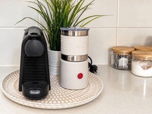 Un plan de travail de cuisine avec un appareil DeLonghi, un récipient Bodum et une plante en pot.