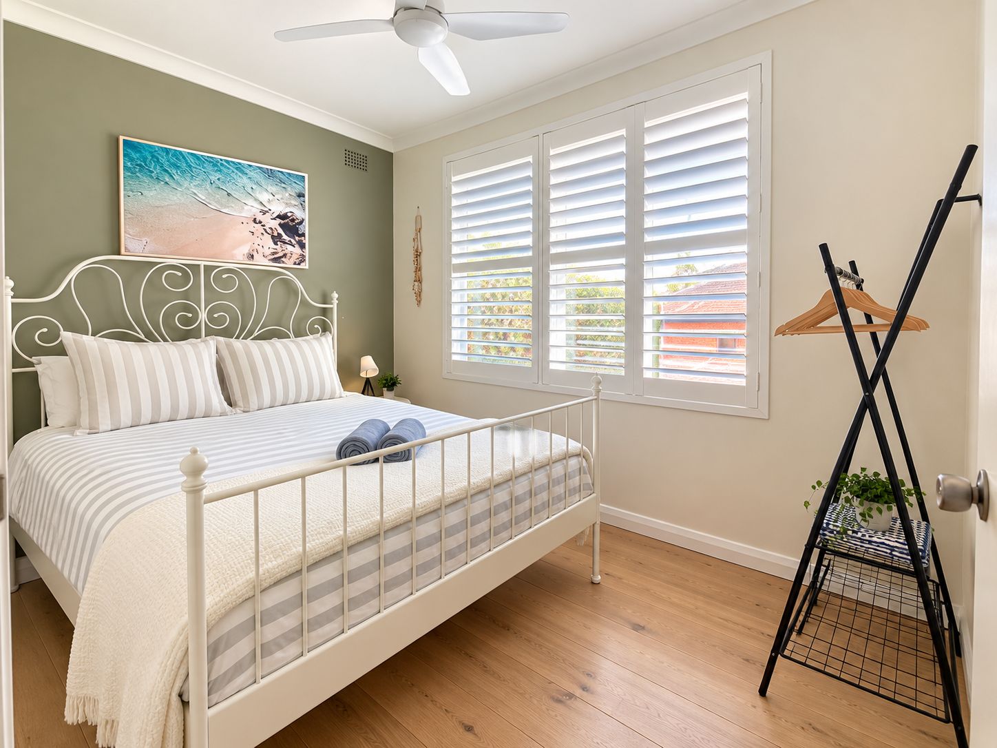 A bedroom with a bed, a ceiling fan, a window with blinds, and a plant on a stand.