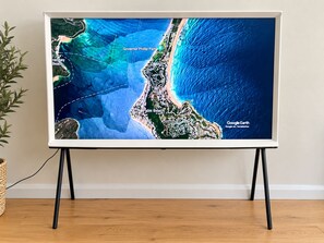 Ein Flachbildfernseher zeigt eine Satellitenansicht einer Küstenregion mit beschrifteten Orten wie Governor Phillip Park und Palm Beach.