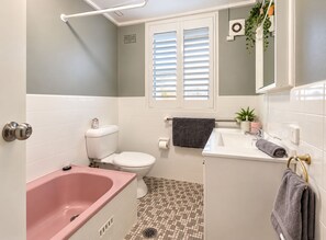 Ein Badezimmer mit einer rosa Badewanne, einer weißen Toilette und einem Waschbecken mit Spiegel darüber.