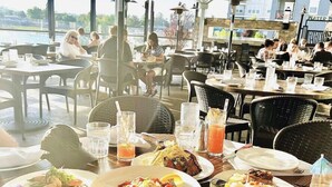 Ein Restaurant mit Außenbereich, verschiedenen Gerichten auf den Tischen und Blick auf das Wasser.