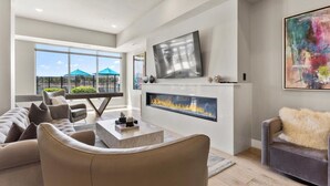 Ein modernes Wohnzimmer mit Kamin, bequemen Sitzgelegenheiten und einem großen Fenster mit Blick ins Freie.