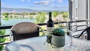 Ein Tisch mit einer Weinflasche, einem Glas und einer Sukkulente auf einem Balkon mit Blick auf einen See und Berge.