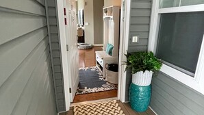 A covered porch with a wooden floor, a green mat, a white bench, a potted plant, and a door leading to an interior space. - Rehoboth Beach Condo w/ Pool Tennis Parking Sleeps 6 (Rehoboth Beach)