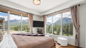 A bedroom with a large bed, a flat-screen TV, and a view of mountains. - Spring Creek 3BR Penthouse ~ Wide Mountain Views ~ (Canmore)