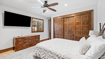 A bedroom with a large bed, wooden wardrobe, ceiling fan, TV, and a window with a view.
