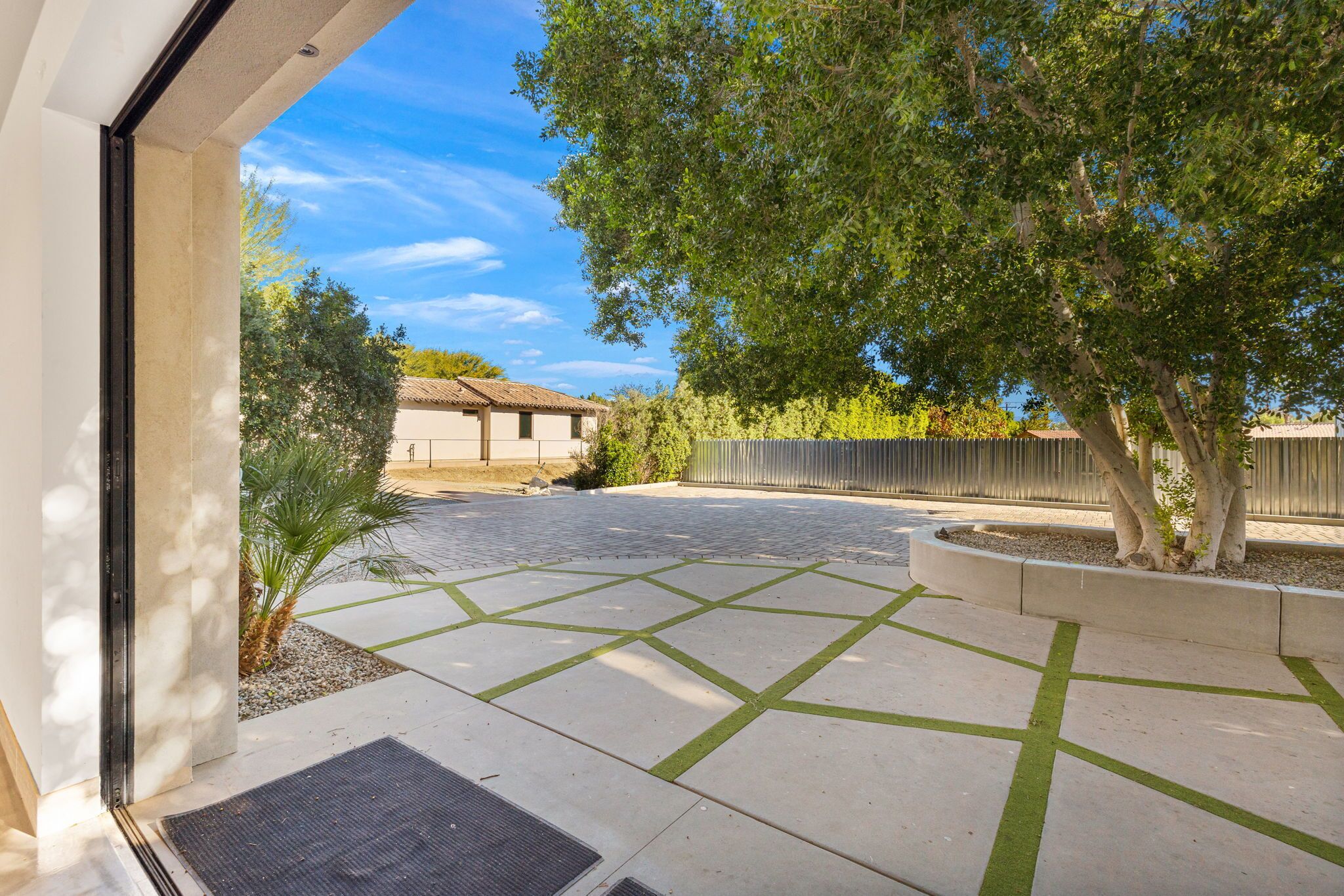 Un patio empedrado con diseños geométricos, un árbol y un edificio al fondo.