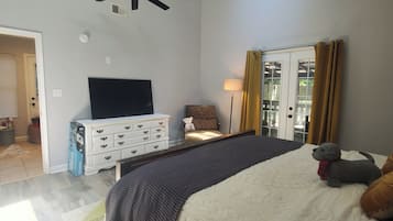 Une chambre avec un grand lit, un ventilateur de plafond, une télévision, une commode et une fenêtre avec des rideaux.