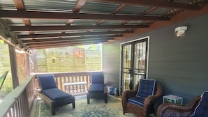 A covered patio area with two blue cushioned chairs, a patterned rug, and a metal-framed door. - Cozy home in quiet neighborhood  (Memphis)