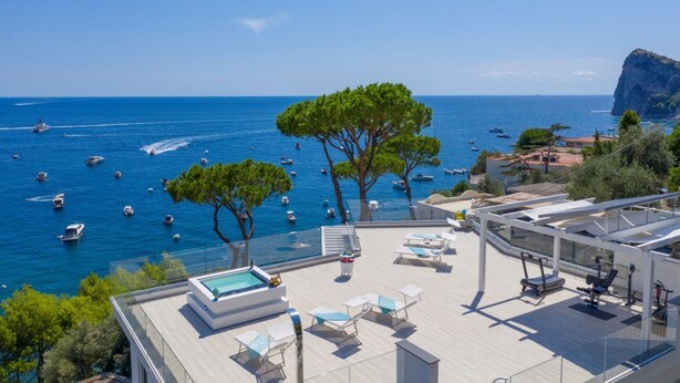 Un área de piscina en la azotea con sillones de descanso, un jacuzzi y vistas al mar con barcos.
