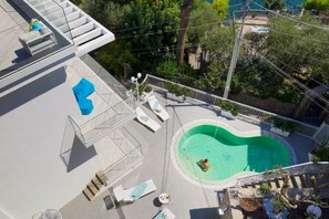 A rooftop pool with lounge chairs, a glass balustrade, and a view of the surrounding landscape.